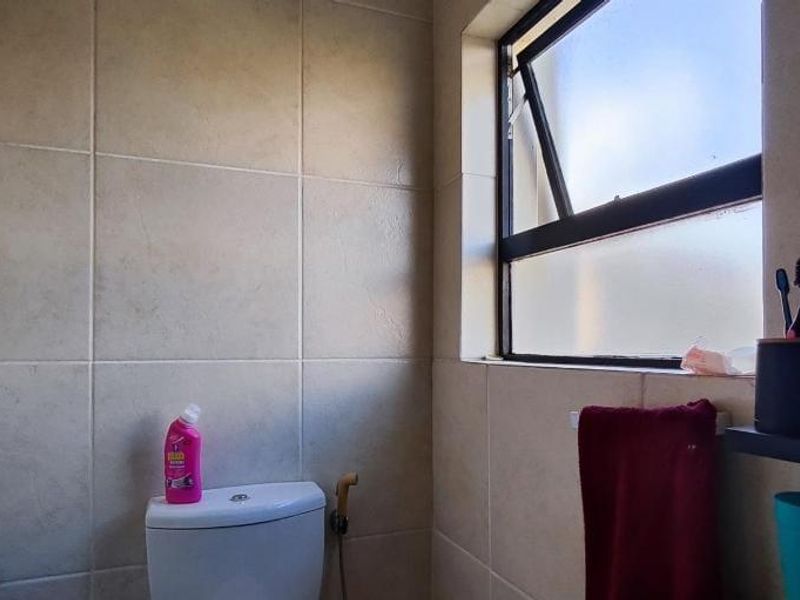 A functional bathroom featuring tiled walls, a standard toilet with a bidet spray, and a top-hung window for ventilation.