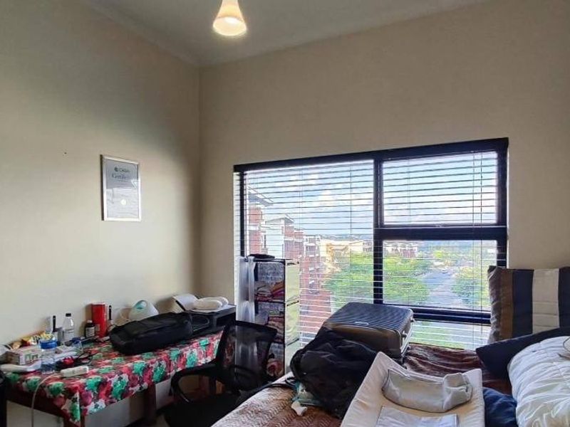 A bedroom featuring a large window with venetian blinds, providing natural light and an exterior view.