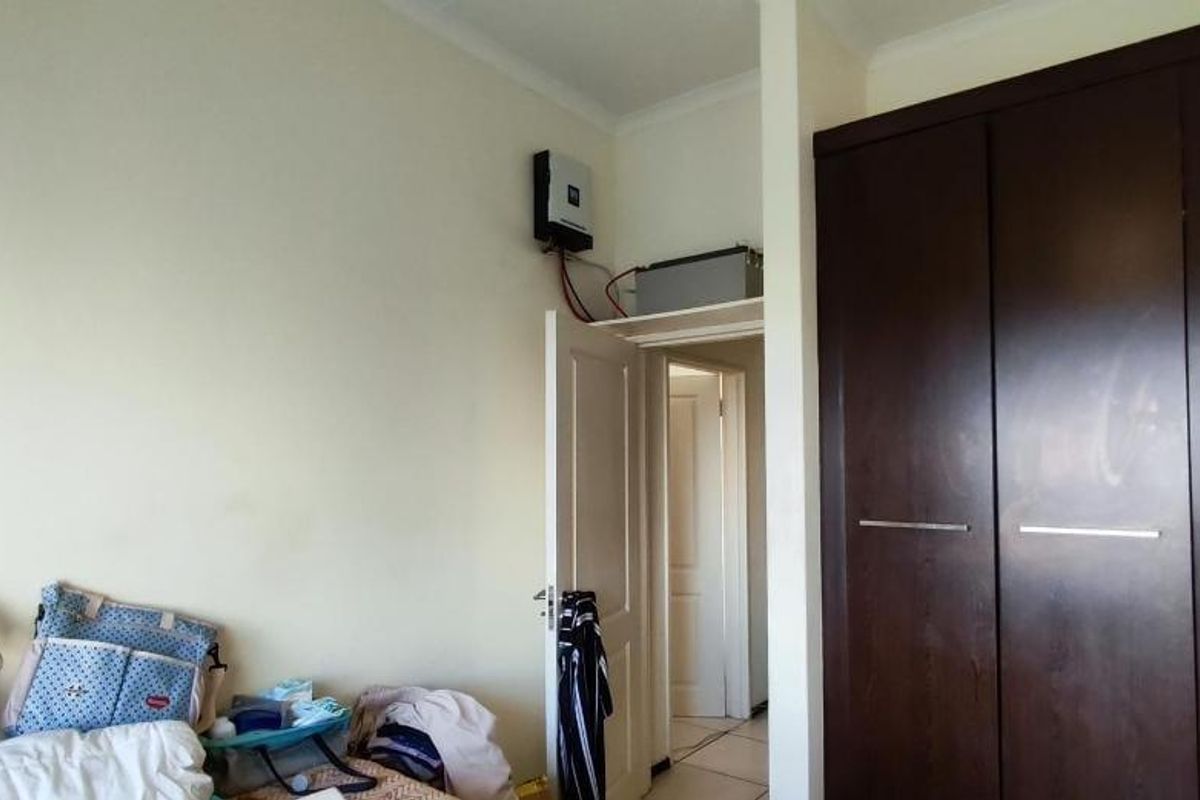 Bedroom featuring dark wood built-in cupboards and a wall-mounted inverter system with battery backup.