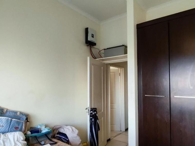 Bedroom featuring dark wood built-in cupboards and a wall-mounted inverter system with battery backup.