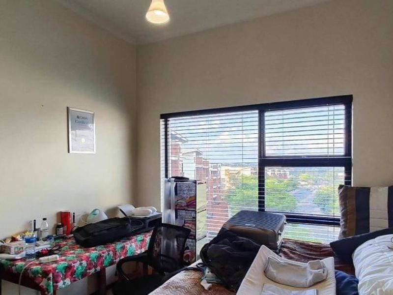 A bedroom featuring a large window with venetian blinds, providing natural light and an elevated view.