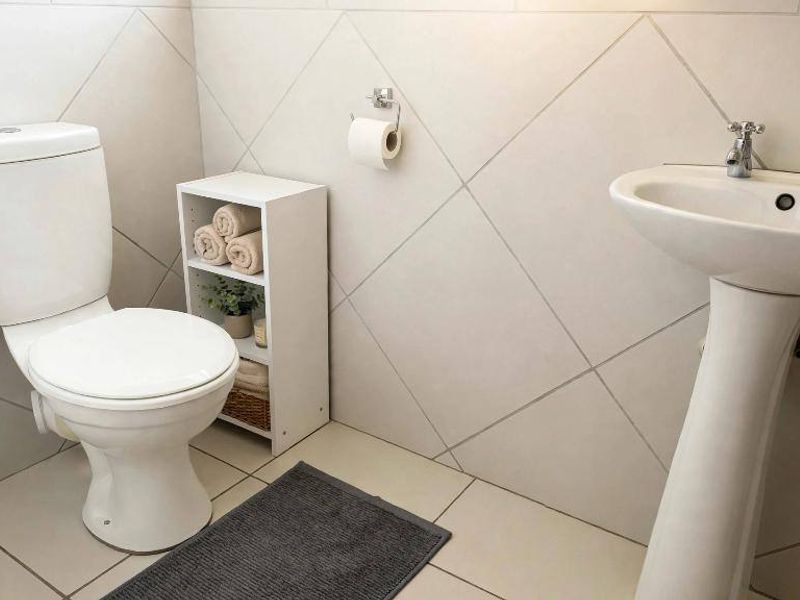 A clean and functional bathroom featuring a white pedestal basin, a standard toilet, and neutral diamond-patterned wall tiling.