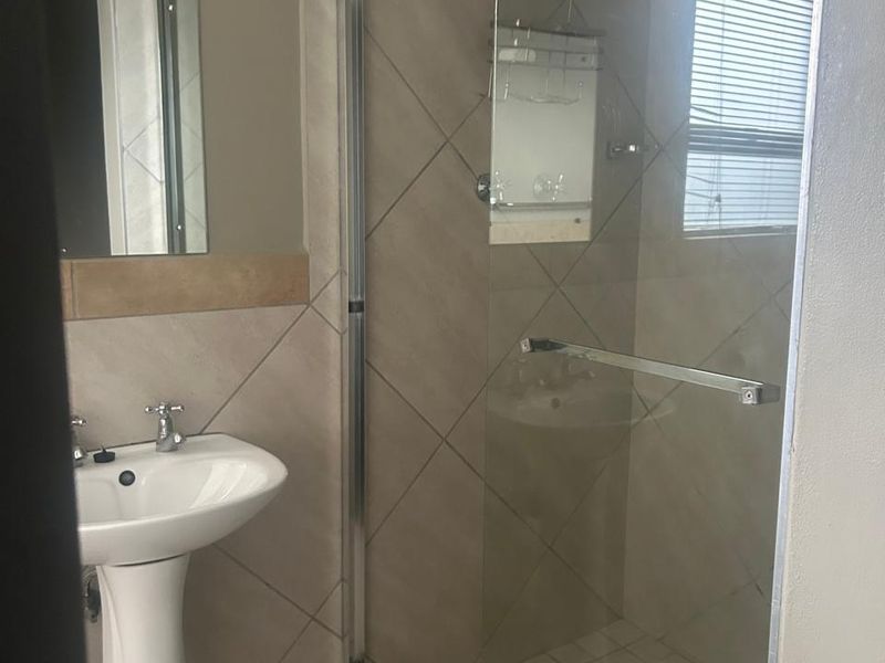 A functional bathroom featuring a pedestal basin, tiled walls, and a glass-enclosed shower with tiled flooring.