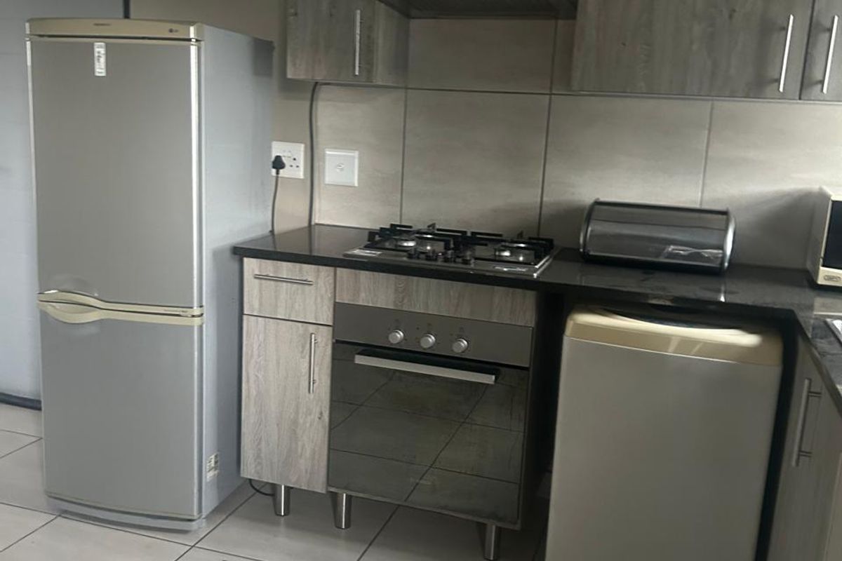 A functional kitchen featuring modern wood-look cabinetry, granite countertops, a gas hob, built-in oven, and an extractor fan with neutral tiled flooring.