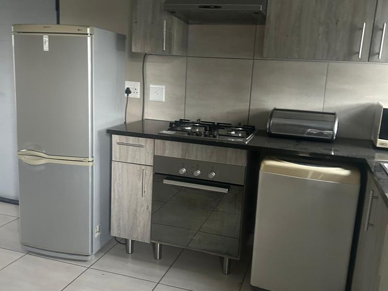 A functional kitchen featuring modern wood-look cabinetry, granite countertops, a gas hob, built-in oven, and an extractor fan with neutral tiled flooring.