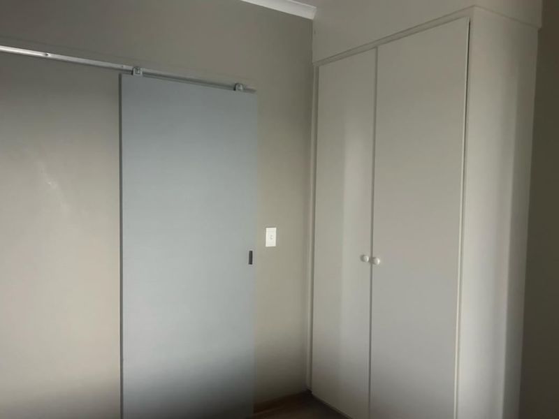 A clean bedroom interior featuring a built-in wardrobe and a modern sliding door, offering a neutral and functional space.