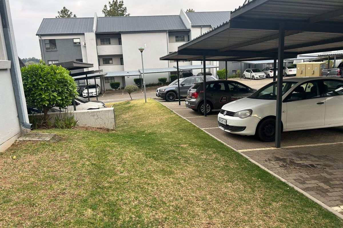 Exterior view of the apartment complex featuring covered parking bays, paved driveway, and a maintained lawn area.