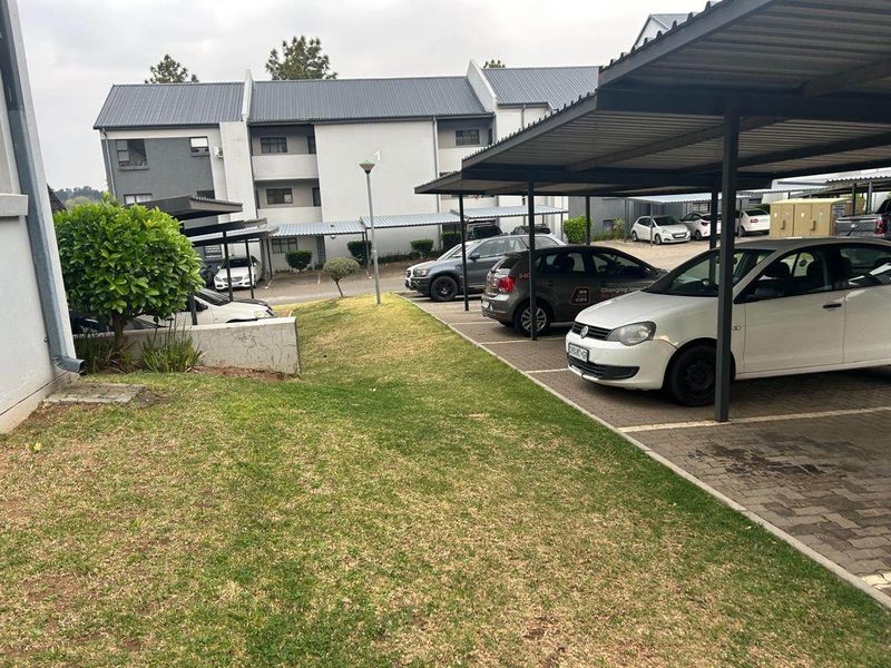 Exterior view of the apartment complex featuring covered parking bays, paved driveway, and a maintained lawn area.