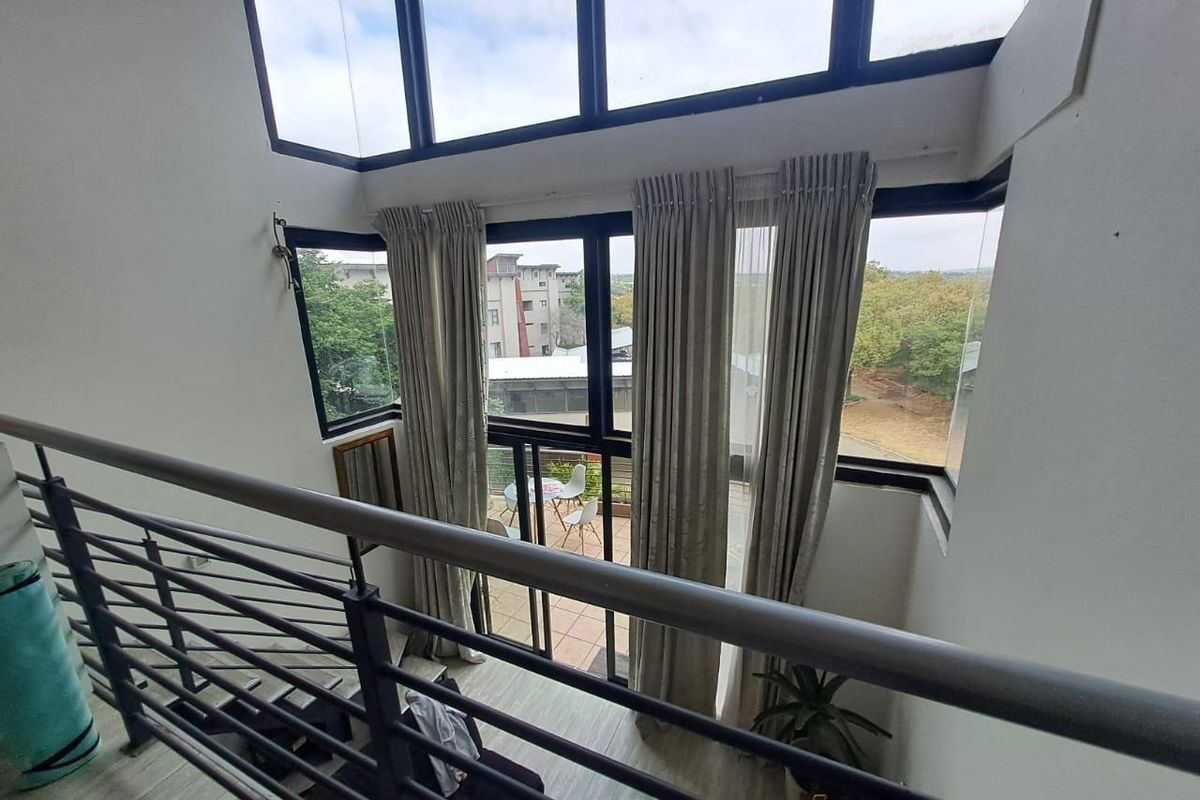 A bright, double-volume living area featuring expansive floor-to-ceiling windows, a modern metal balustrade, and direct access to an outdoor balcony.