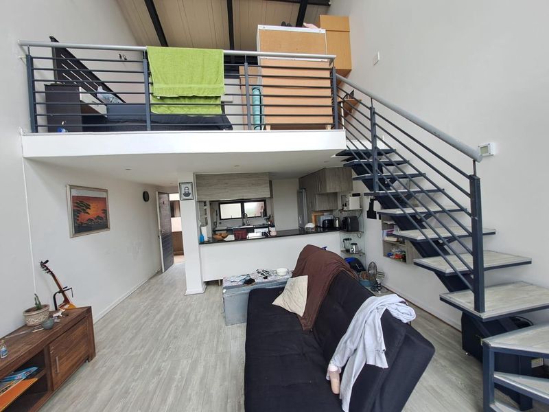 Open-plan living area featuring a mezzanine level, modern metal staircase, and a functional kitchen space with contemporary cabinetry and laminate flooring.
