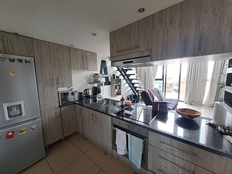 Modern open-plan kitchen featuring wood-grain cabinetry, granite countertops, and integrated appliances, flowing into a living area with a staircase.