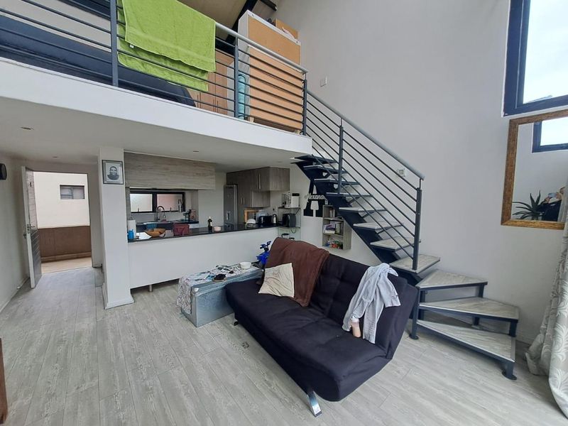 Open plan living area featuring a mezzanine level, modern metal staircase, and a compact kitchen with stone countertops and laminate flooring.