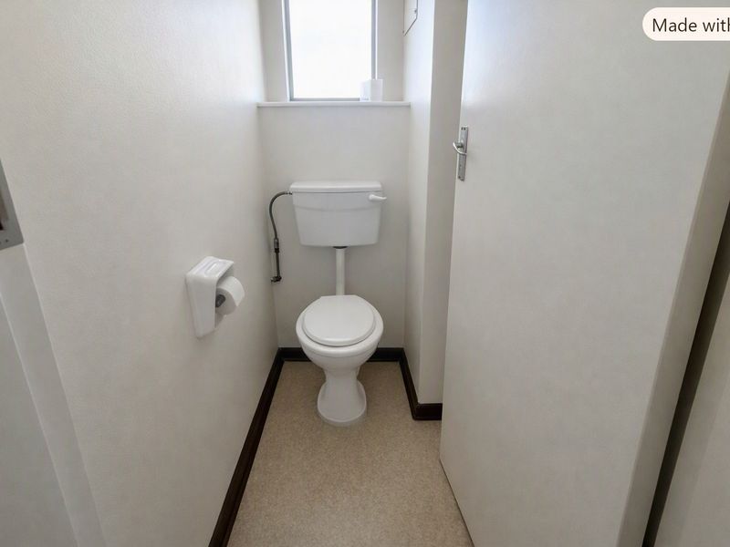 A compact, functional bathroom featuring a standard toilet, neutral finishes, and a small window for natural light.