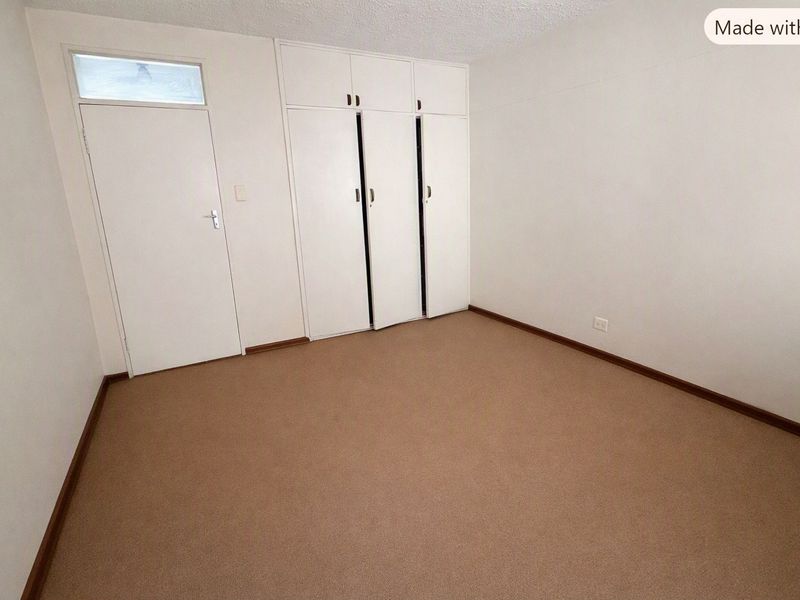 An empty bedroom featuring neutral carpeting, built-in storage cupboards, and a classic door with a transom window above.