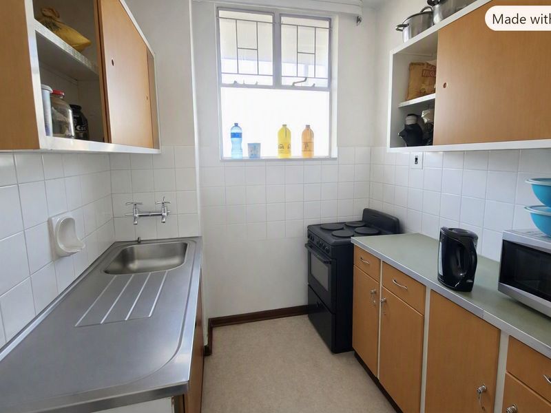 A compact, functional kitchen featuring dated wooden cabinetry, a stainless steel sink, tiled splashbacks, and a freestanding stove.