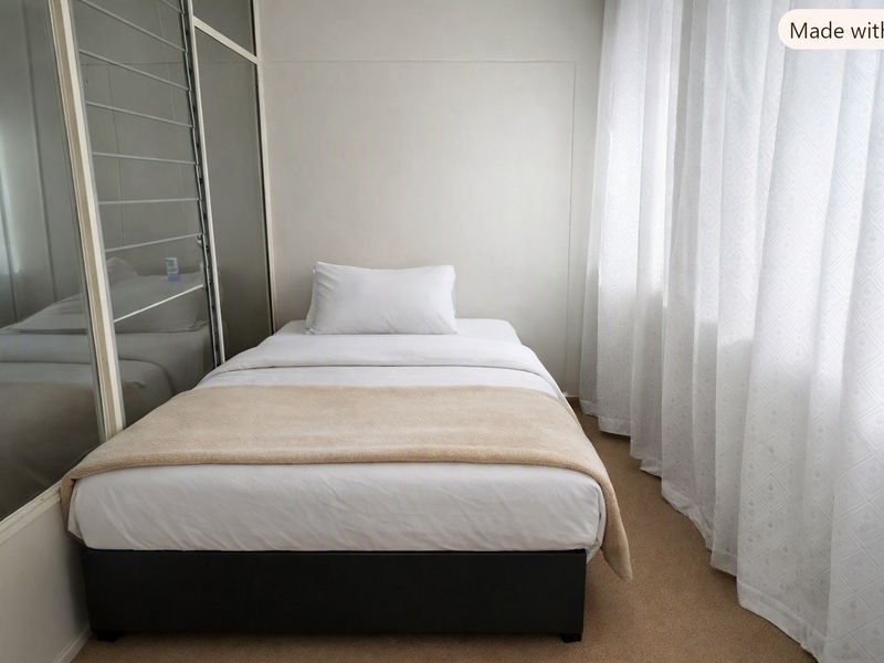 A compact bedroom featuring neutral carpet flooring and a built-in sliding door wardrobe with mirrored panels.
