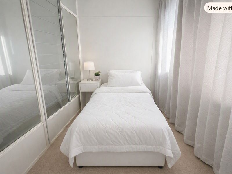 A compact bedroom featuring neutral carpet flooring and a large built-in sliding door wardrobe with mirrored panels.