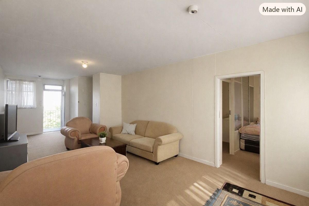 A neutrally painted living room featuring carpeted flooring, a sliding glass door leading to a balcony, and access to an adjacent bedroom.