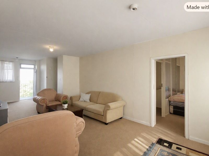 A neutrally painted living room featuring carpeted flooring, a sliding glass door leading to a balcony, and access to an adjacent bedroom.
