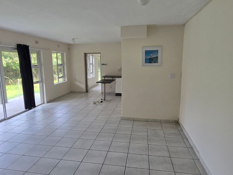 Spacious open-plan living area featuring neutral tiled flooring, large sliding glass doors providing garden access, and a functional built-in breakfast bar.