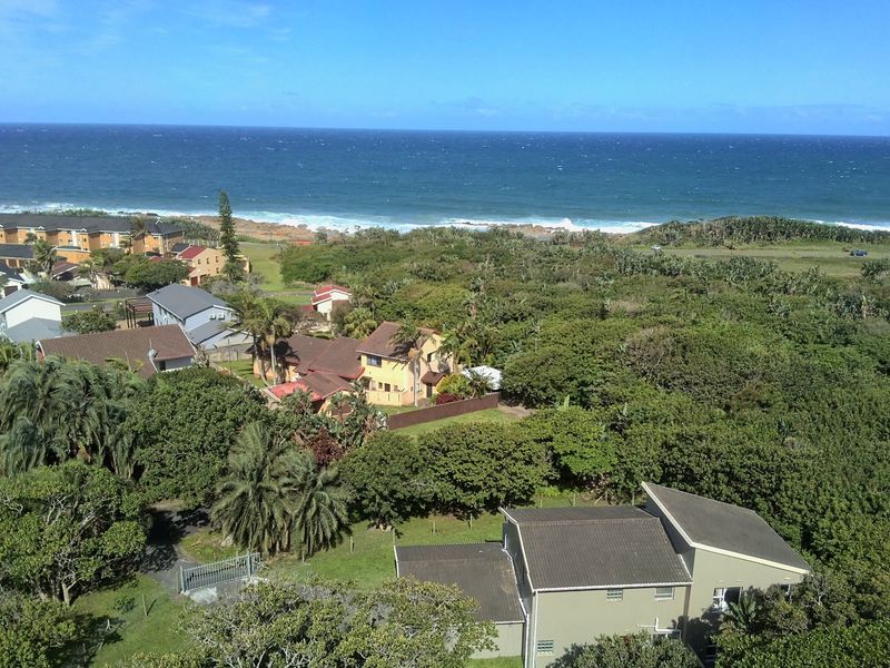 An aerial view of the coastal residential property, showcasing the surrounding neighborhood, lush vegetation, and proximity to the ocean.