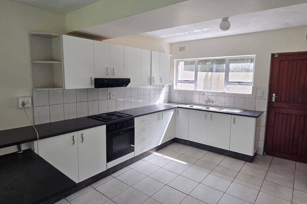 A functional kitchen featuring white built-in cabinetry, dark laminate countertops, an integrated stove and oven, and tiled flooring with direct exterior access.