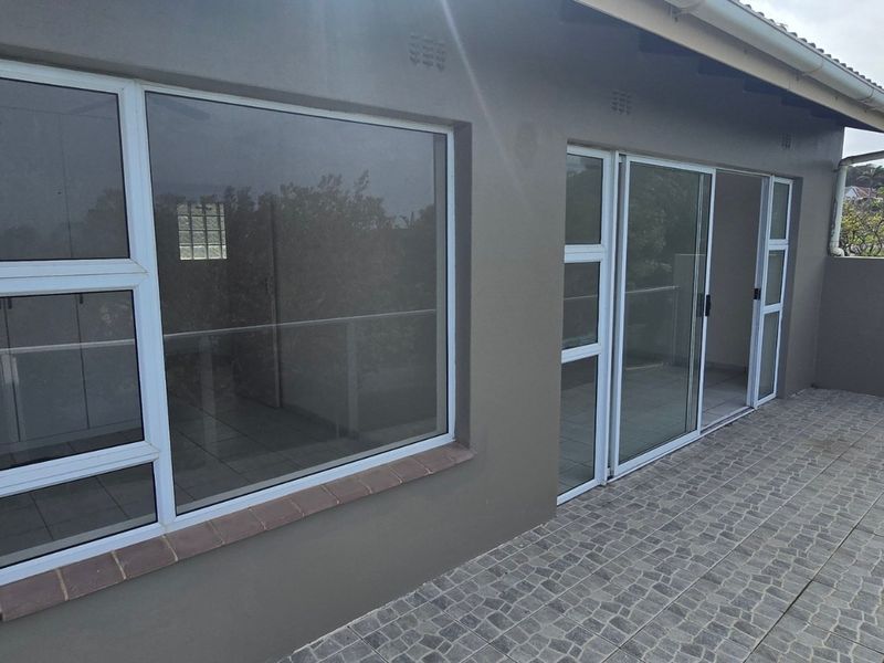 A spacious covered balcony featuring modern tiled flooring, glass balustrades, and large sliding glass doors providing access to the interior living space.
