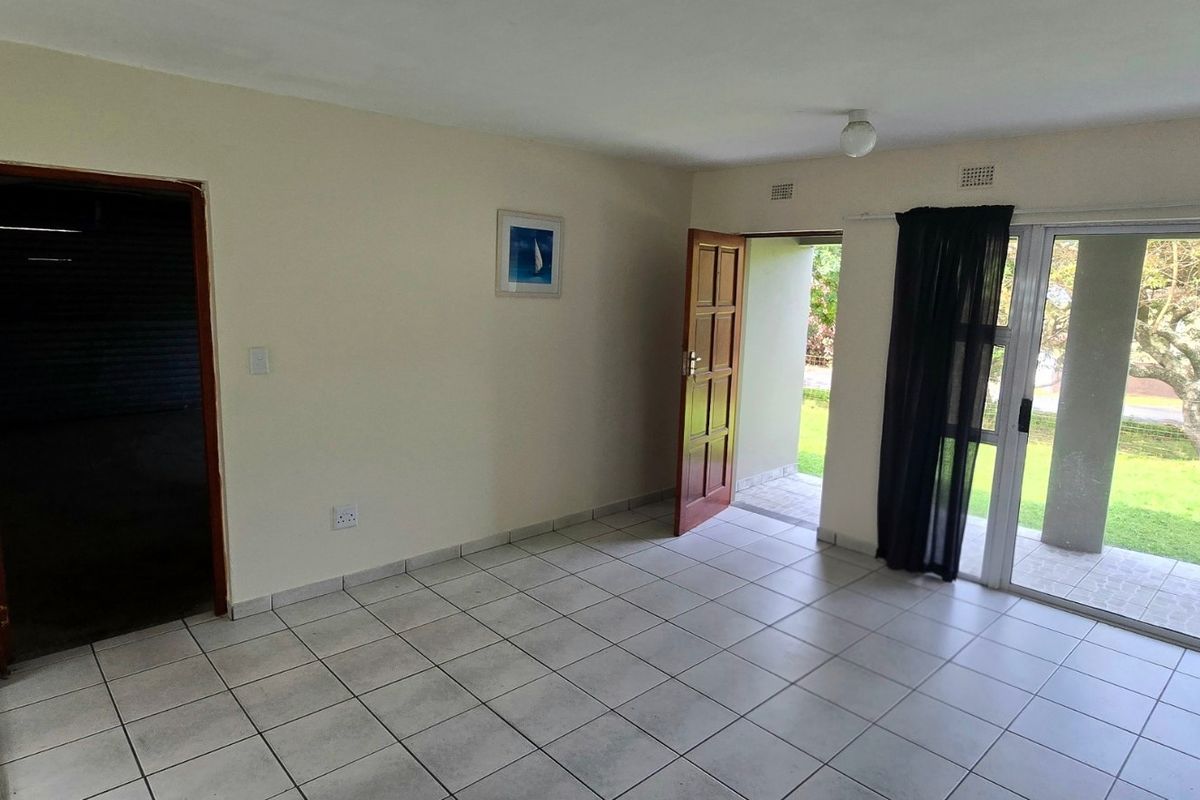 An empty living room featuring tiled flooring, a timber door, and large sliding glass doors providing access to the outdoor garden area.