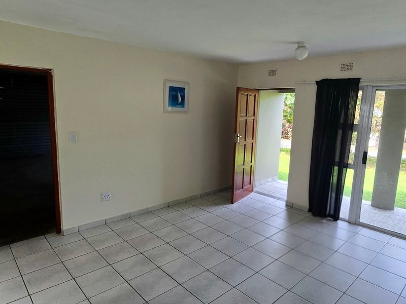 An empty living room featuring tiled flooring, a timber door, and large sliding glass doors providing access to the outdoor garden area.