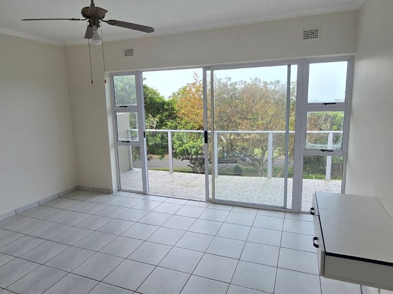 Spacious bedroom featuring neutral tiled flooring, a ceiling fan, and large sliding glass doors providing direct access to a private balcony.