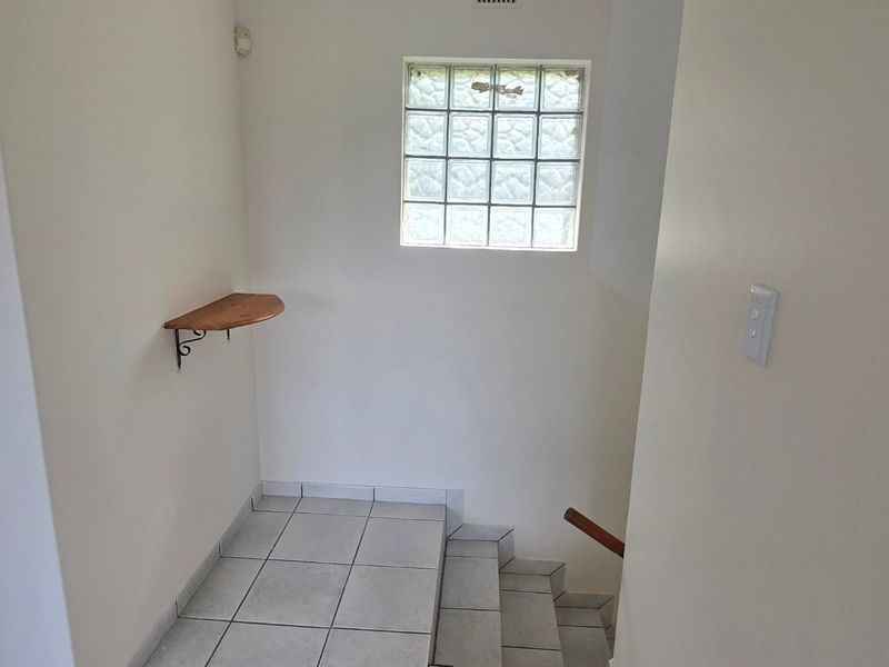 A functional hallway area featuring ceramic floor tiles, a glass block window, and a staircase leading to another level.