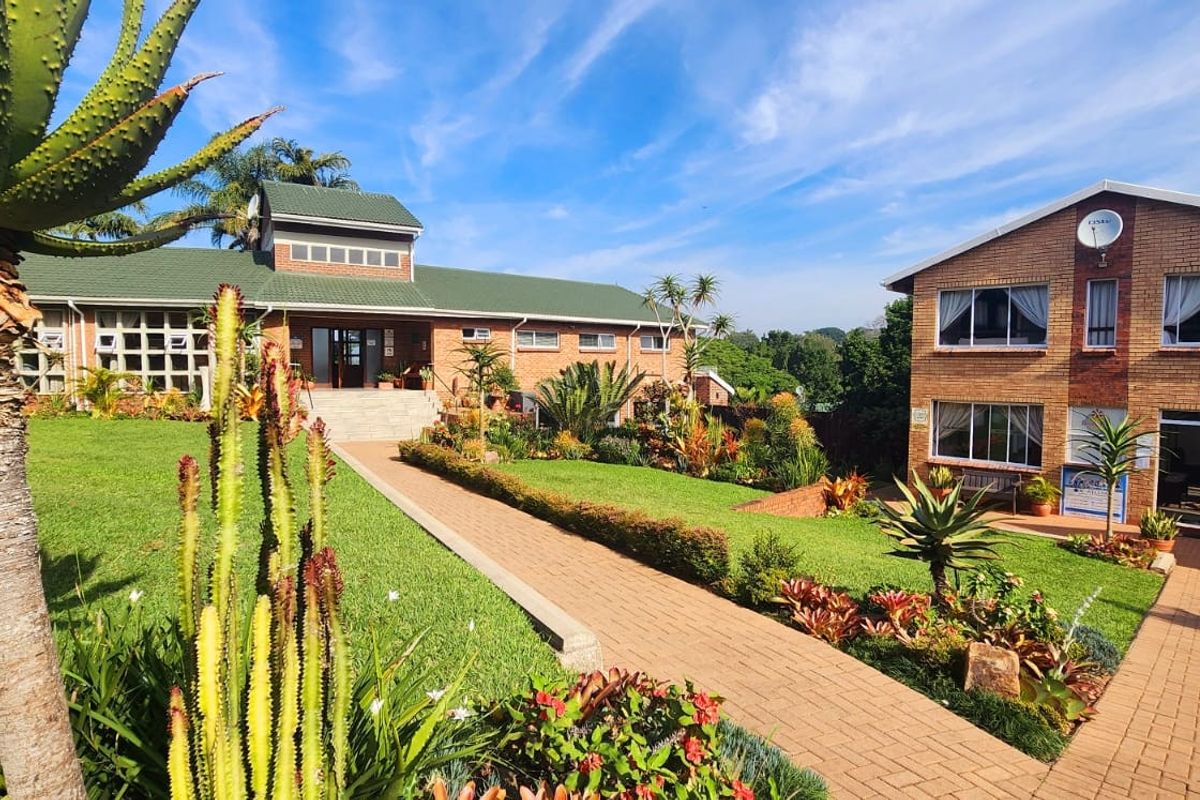 A well-maintained commercial property exterior featuring brick buildings, green tiled roofs, paved walkways, and established landscaped gardens.
