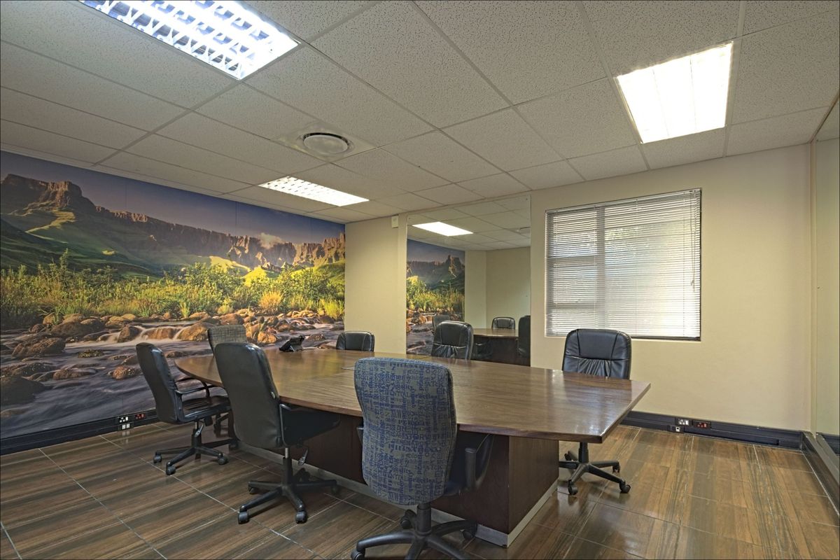 A professional office meeting room featuring a large boardroom table, suspended ceiling with recessed lighting, tiled flooring, and a decorative landscape wall mural.