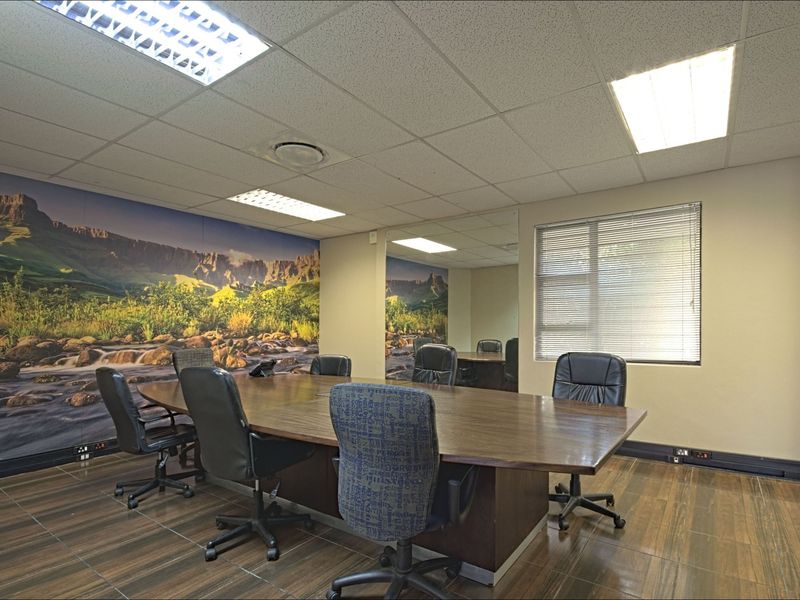 A professional office meeting room featuring a large boardroom table, suspended ceiling with recessed lighting, tiled flooring, and a decorative landscape wall mural.