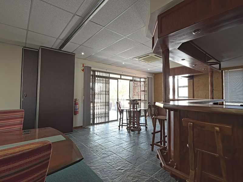 A commercial bar area featuring a built-in wooden counter, slate flooring, and direct access to an outdoor space through sliding security doors.