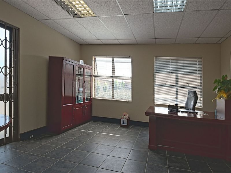 A functional commercial office space featuring tiled flooring, a suspended ceiling with recessed lighting, and secure window access.
