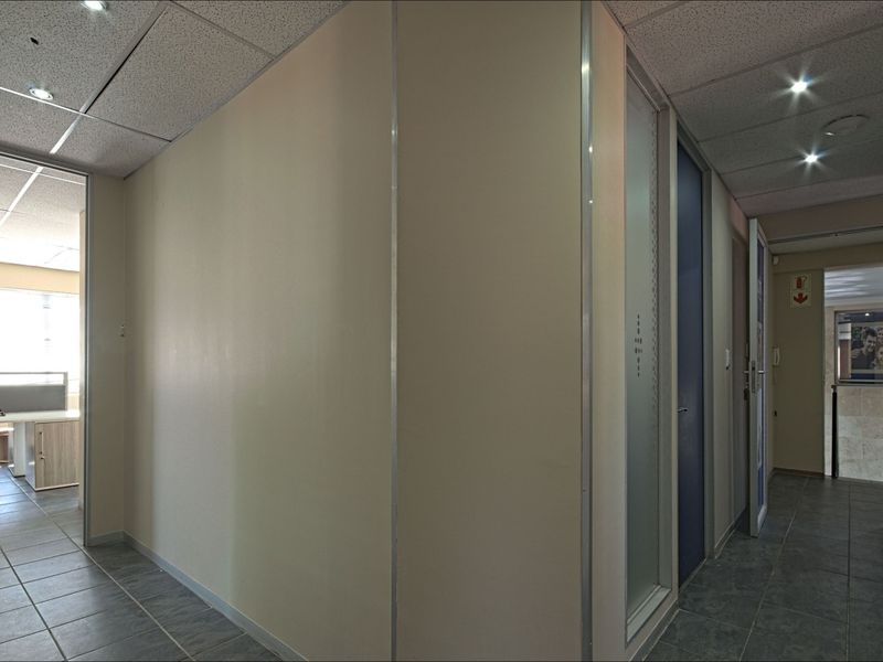 A clean commercial hallway featuring tiled flooring, suspended ceilings with recessed lighting, and multiple access points to adjacent office spaces.