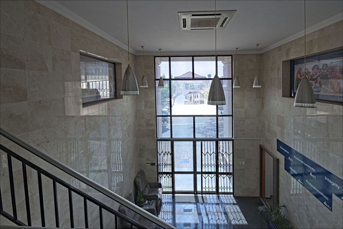 Spacious commercial entrance foyer featuring high ceilings, stone wall cladding, large glass facade, and a metal staircase.