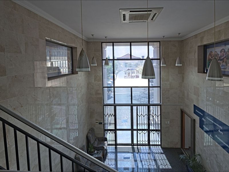 Spacious commercial entrance foyer featuring high ceilings, stone wall cladding, large glass facade, and a metal staircase.