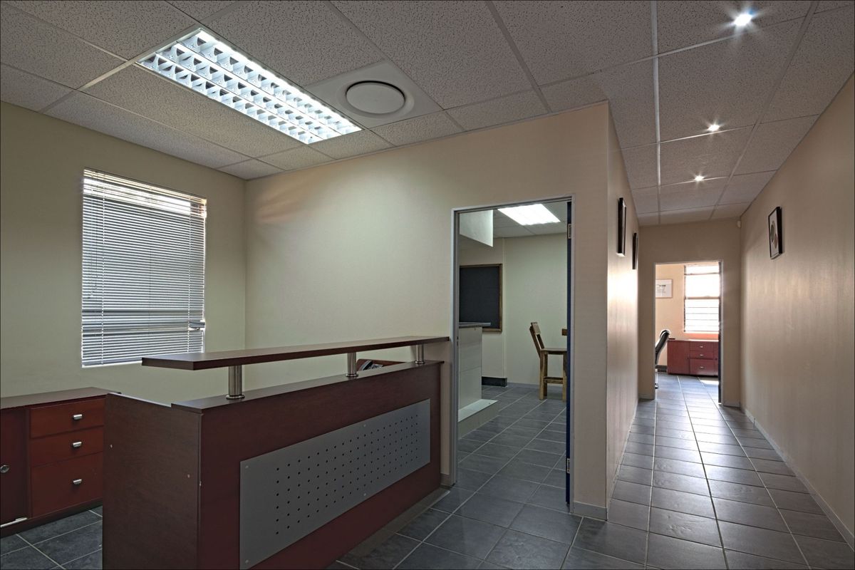 Commercial office space featuring tiled flooring, a built-in reception desk, suspended ceilings with recessed lighting, and natural light through venetian blinds.