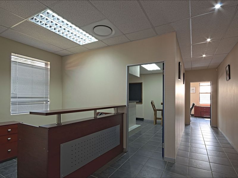 Commercial office space featuring tiled flooring, a built-in reception desk, suspended ceilings with recessed lighting, and natural light through venetian blinds.