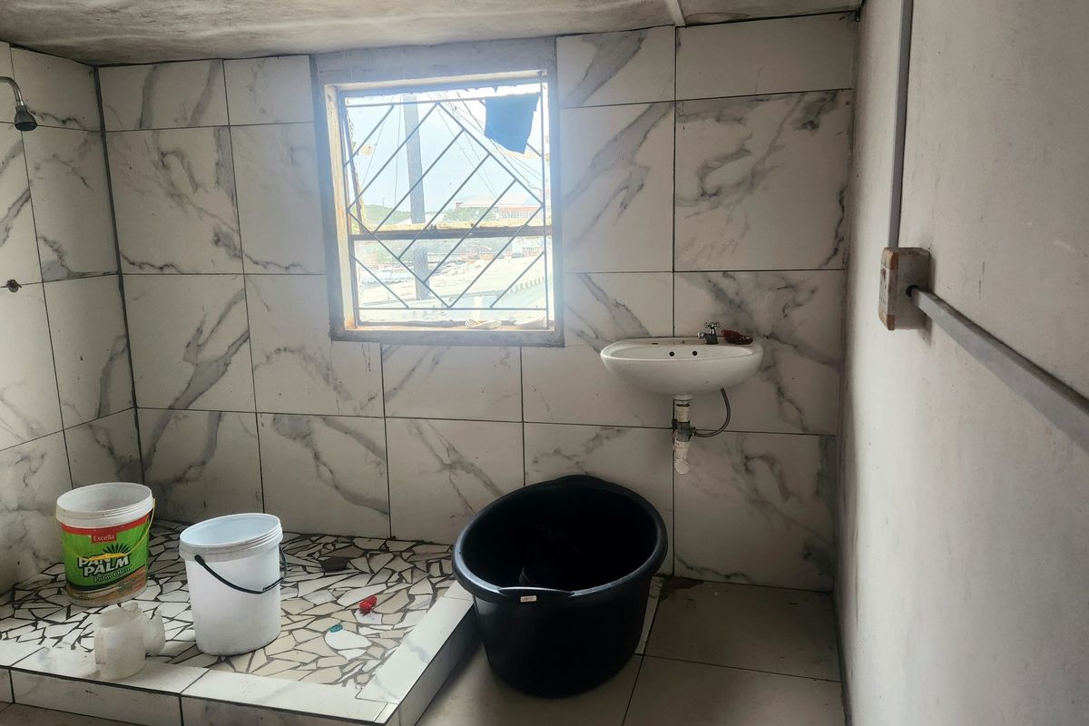 A basic bathroom featuring marble-effect wall tiles, a wall-mounted basin, and a tiled shower area, currently requiring significant renovation and finishing.