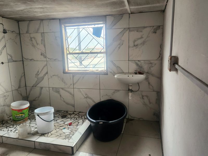 A basic bathroom featuring marble-effect wall tiles, a wall-mounted basin, and a tiled shower area, currently requiring significant renovation and finishing.