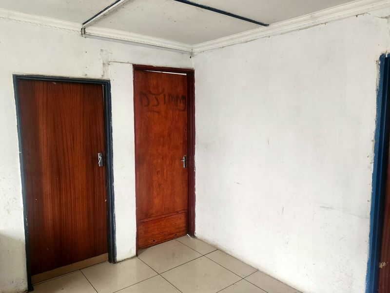 A vacant hallway featuring tiled flooring and wooden doors, currently showing signs of wear and requiring cosmetic maintenance.
