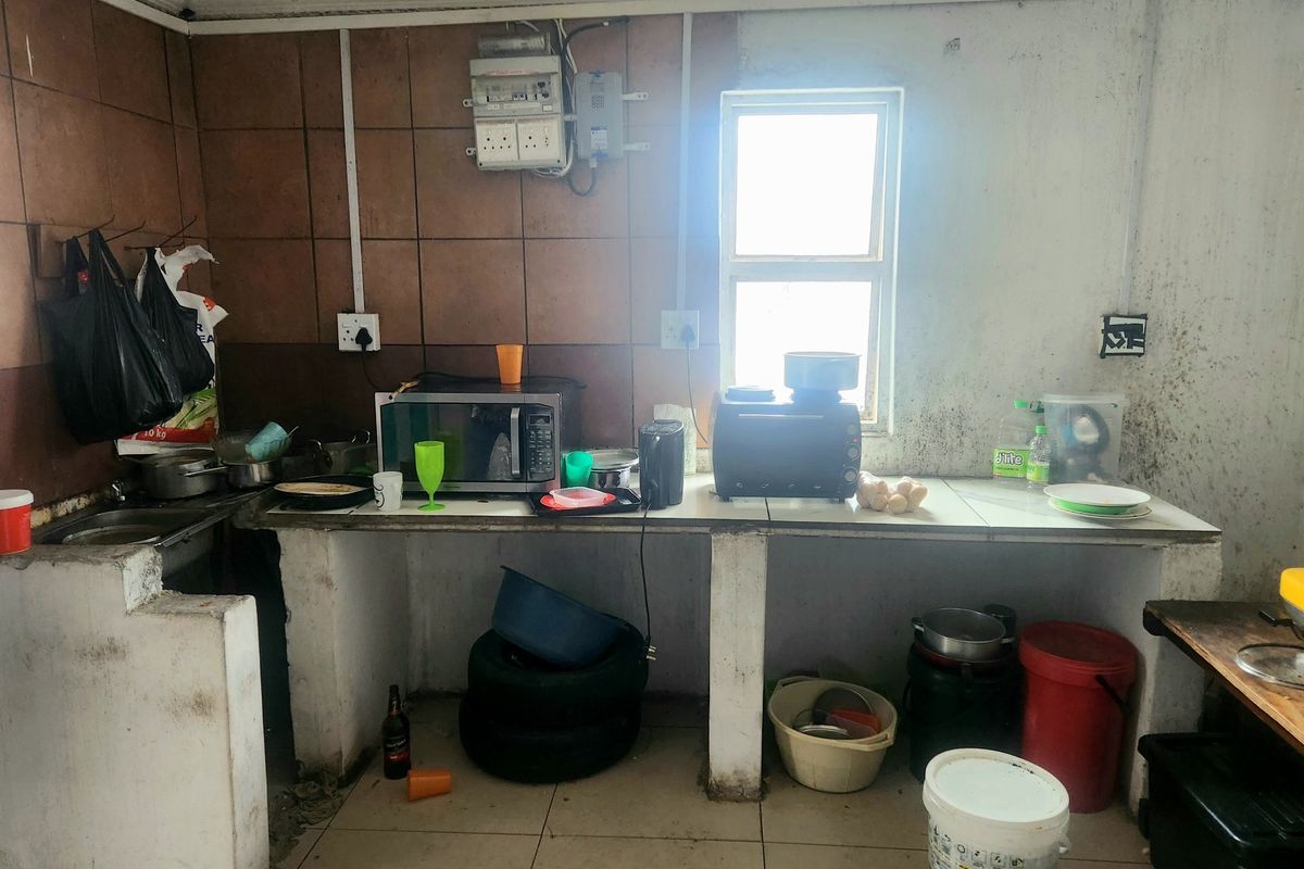 A basic kitchen area featuring concrete countertops, tiled splashbacks, and a built-in sink, requiring significant maintenance and cosmetic updates.