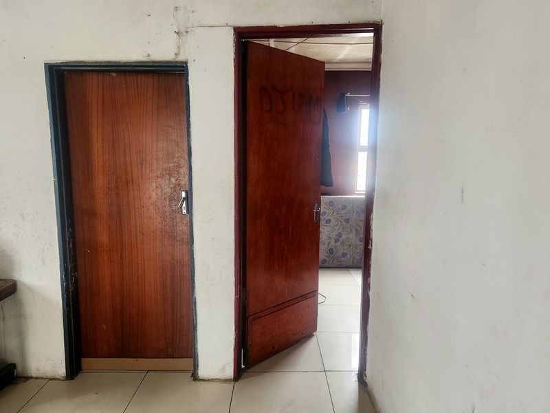 A narrow hallway featuring tiled flooring and two wooden doors, showing signs of wear and requiring cosmetic attention.