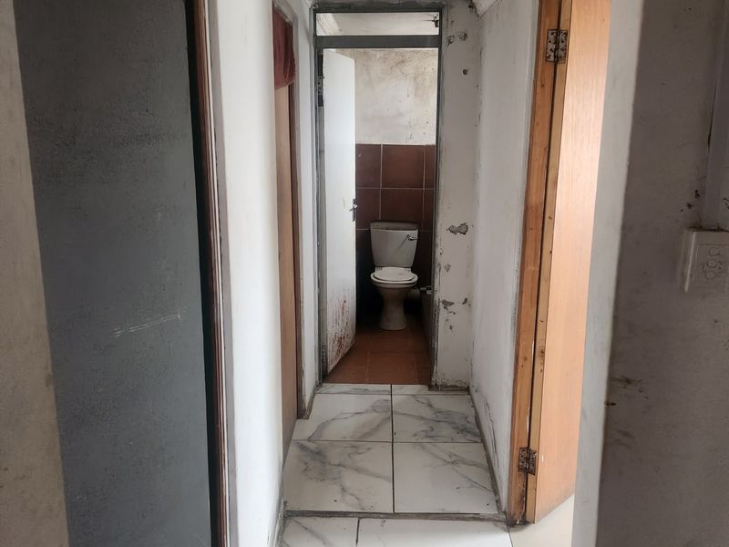 A narrow hallway with tiled flooring leading to a bathroom, showing signs of wear and requiring cosmetic updates to the walls and finishes.