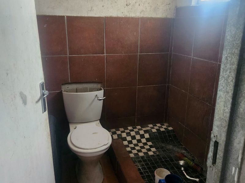 A small, dated bathroom featuring a toilet and floor drain, requiring significant renovation and cosmetic updates to improve its condition and functionality.