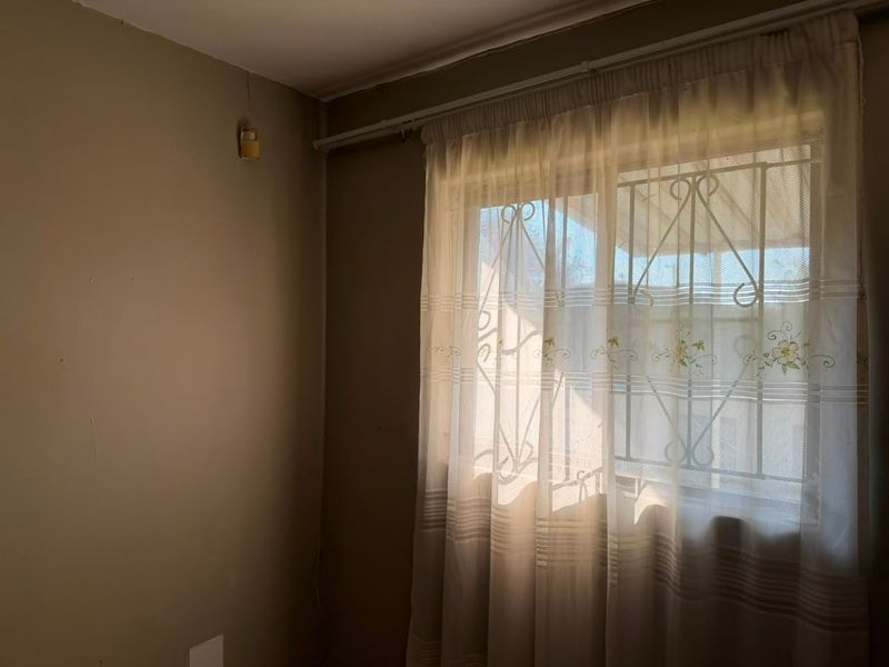A simple bedroom featuring a window with a security gate and an installed alarm sensor, providing a functional and secure space.