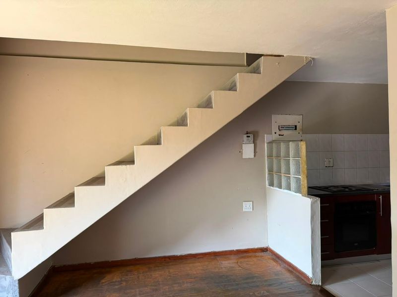 Open plan living area featuring a staircase, glass block partition, and a compact kitchen corner with built-in oven and hob.
